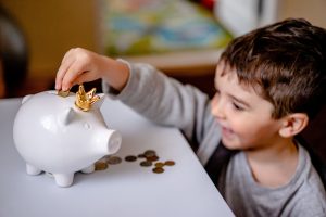 A boy putting a coin in a piggy bank. Psychology of money.